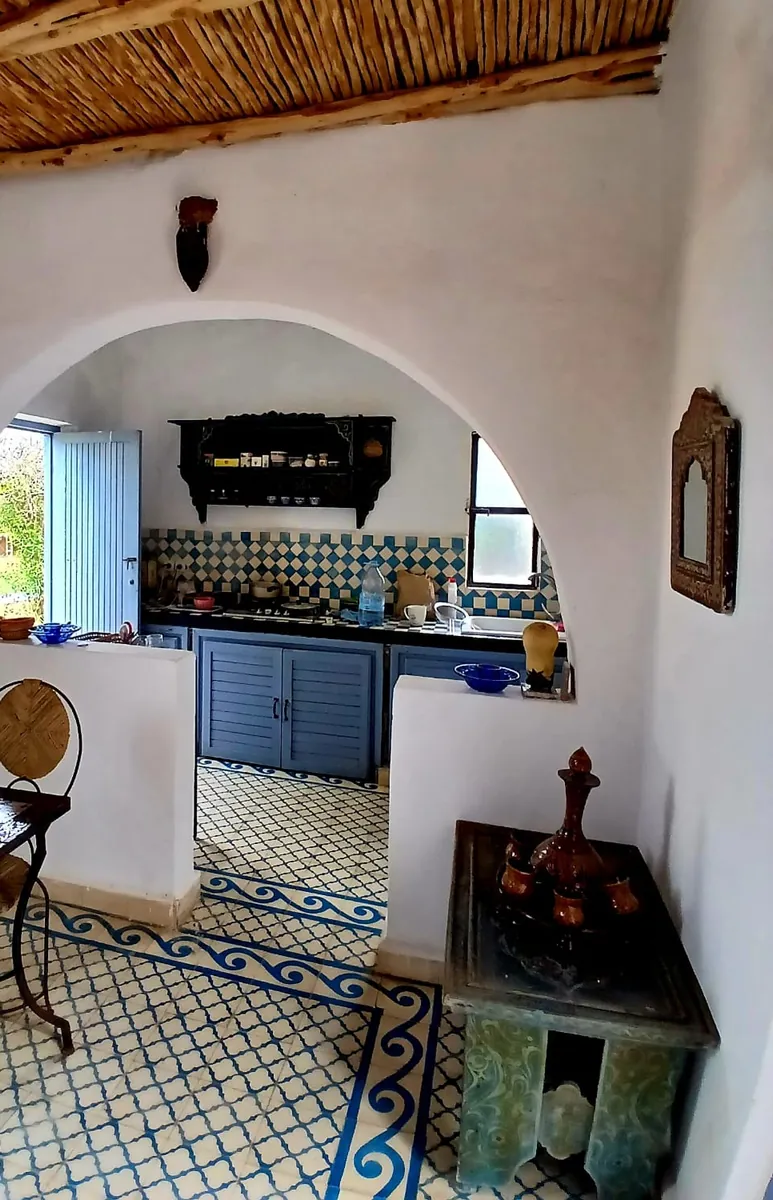 La cuisine vue sous une arche blanche, placards bleus et crédence de carreaux bleus et blancs.